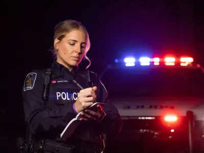 Female officer writing in notebook, at night, cruiser lights flashing in background